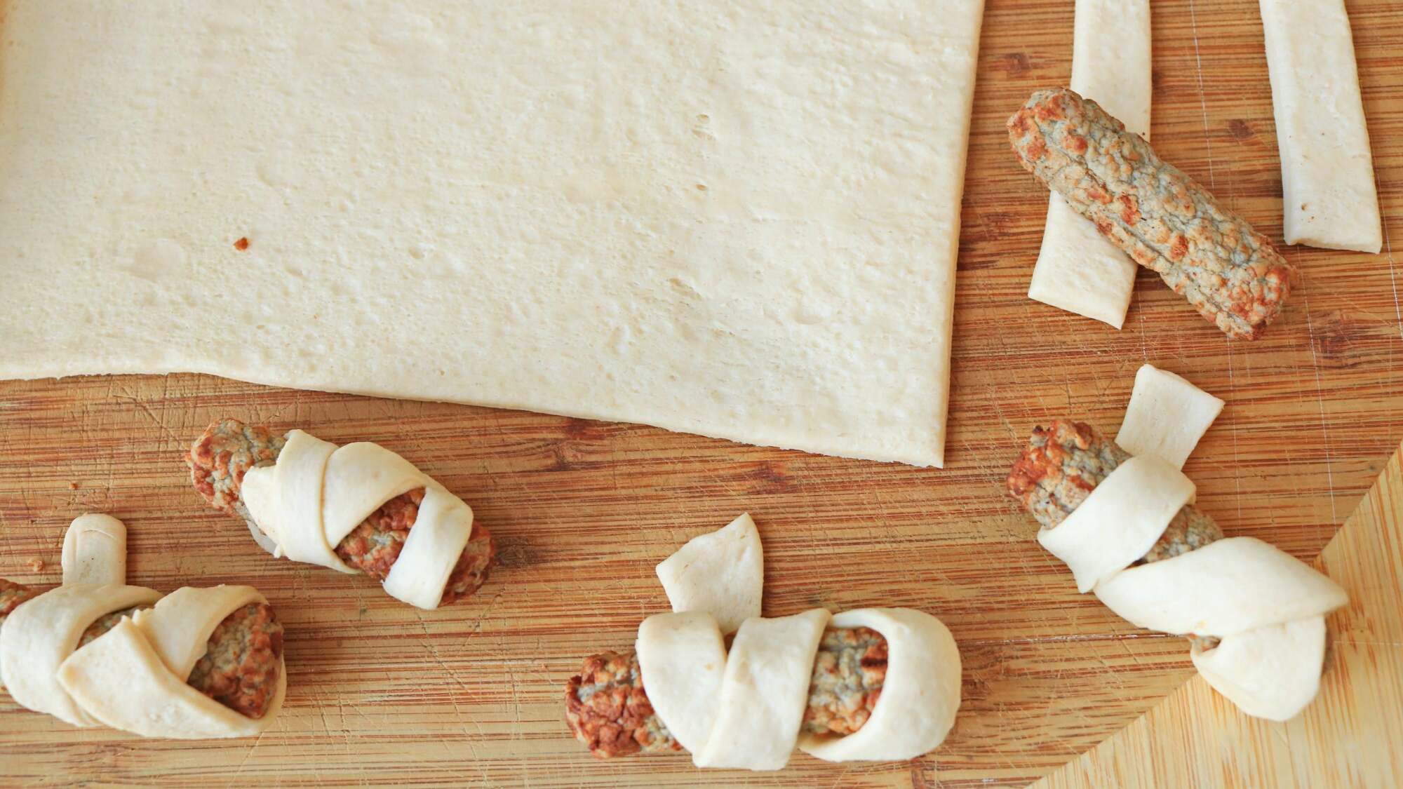 Small sausages wrapped in raw crescent dough on a cutting board.